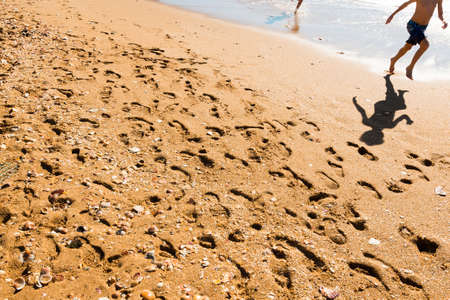 Two unrecognizable happy kids jumping on the beach with reflections in great sunlightの写真素材