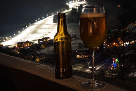Glass and bottle with craft beer on a balcony at skiing villageの写真素材