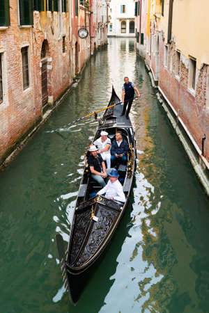 Venetian gondolier punting gondola through green canal waters of Venice, Italyのeditorial素材