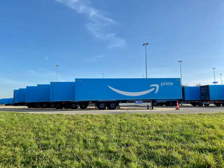 Multiple blue Amazon prime trailers are parked within a waiting are close to the airport ready for...