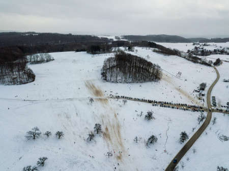 Aerial view of people enjoying a winter day by sledding on a small ski slope during winter holidays in a small village on the Swabian Alps in Southern Germny. The ski lift is not operating due to the pandemic during the winter of 2020/2021.の写真素材