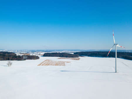 Aerial view of wind turbine in snow covered landscape in rural Germany on a sunny winter day with great blue sky and shadow visible on the snowの写真素材