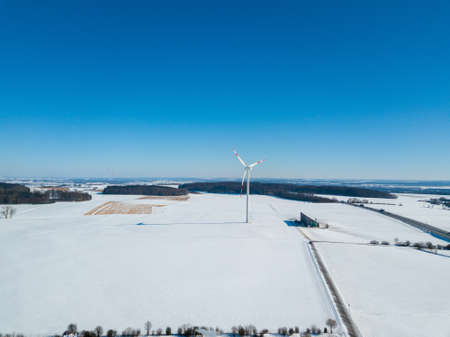 Aerial view of wind turbine in snow covered landscape next to highway A8 near Ulm in Southern Germany on a sunny winter day with great blue sky and shadow visible on the snowの写真素材