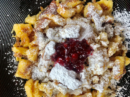 A top view of Kaiserschmarrn - a typical Austrian dessert with torn pancakes, cranberries jam and icing sugar on a dark plate.の写真素材