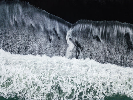 Aerial of turquoise ocean waves crashing against the dramatic black sands of Reynisfjara beach in Iceland highlight the raw power of natureの写真素材