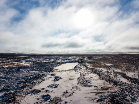 Aerial of snow covering the volcanic landscape near Dettifoss Waterfall in Iceland, creating a serene winter scene under a cloudy skyの写真素材