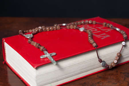 Red Bible and wooden rosary on a table. Black backgroundの写真素材