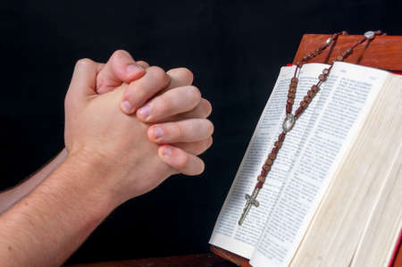 Hands praying in front of a Bible and a rosaryの写真素材