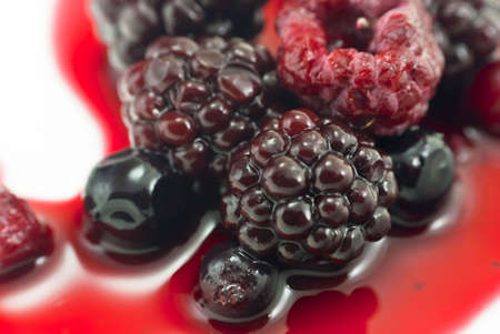 Closeup of Summer berry fruits on a white plate, bathed in natural berry juice.  Includes blackberries, raspberries, blackcurrants and redcurrants.の写真素材