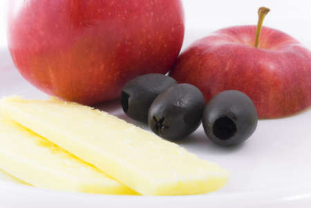 Red apple, black olives and cheddar cheese on white china plate.の写真素材