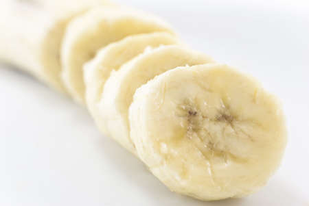 Close-up of sliced banana seated diagonally across frame with white background on either side.  Main portion in soft focus in the background.の写真素材