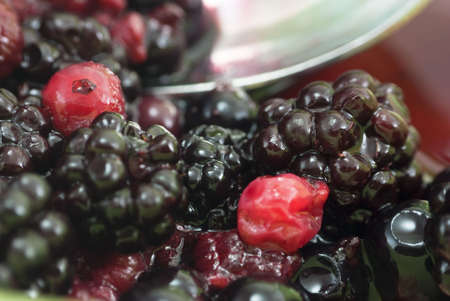 Closeup shot of summer fruits in a bowl, comprising blackberries, raspberries, redcurrants and blackcurrants in their own juice.  A spoon scoops some berries in soft focus in the background.の写真素材
