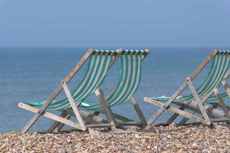 Green and white striped wooden deckchairs, facing the sea on a pebble beach.  Sunny day.の写真素材