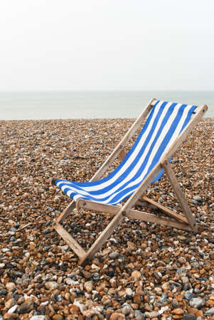 Vertical (portrait) shot of a solitary deckchair on a pebble beach, on a grey day.の写真素材
