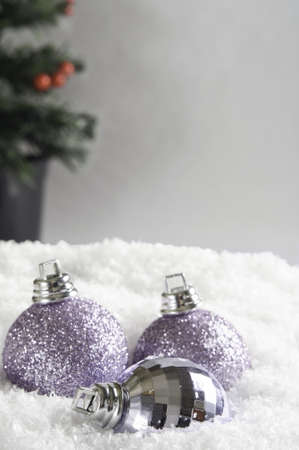 Three Christmas baubles, partly submerged in white snow.  Grey background provides copy space above and right with Christmas tree in soft focus.の写真素材