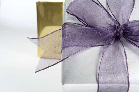 Close up (macro) of a gift box wrapped in silver paper with purple organza ribbon tied in a bow.  A...