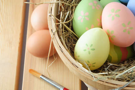 Close up of hand painted Easter eggs in a basket filled with straw with natural, unpainted eggs and...