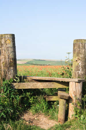 A country stile, leading to a poppy field and farmland beyond.  の写真素材