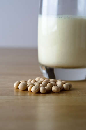 Dry soya (soy) beans with glass of soya milk in soft focus background on a light wooden table.の写真素材
