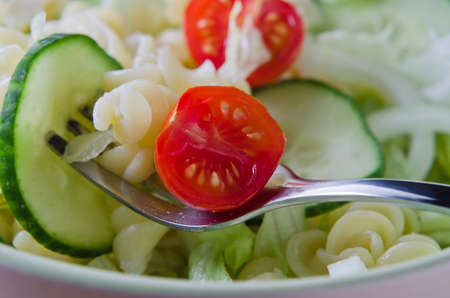Close up (macro) of a fork, lifting pasta and salad from a bowl.  Landscape (horizontal) orientation.の写真素材