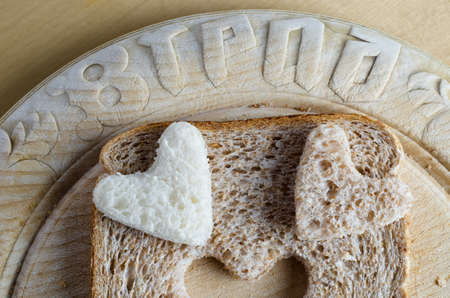 Close up of white and brown wholemeal bread hearts and slice on an old vintage bread board with the word 'bread' embossed in the wood.  の写真素材