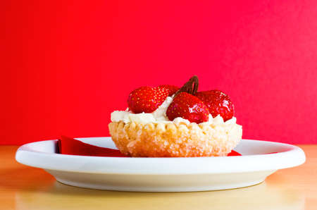 A strawberry and cream pastry cake with chocolate decoration on red napkin and white plate, against a red background.の写真素材