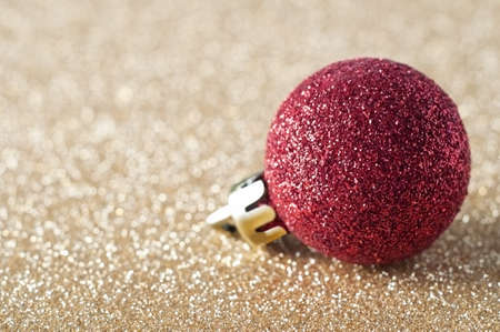 A single, sparkly red bauble, coated in glitter, resting on a gold glitter background that softens into soft focus bokeh in the background.  Copy space to left.の写真素材