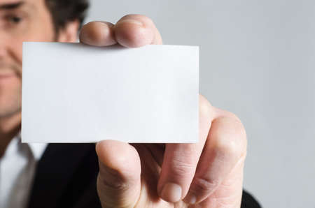 A man in a black suit with white shirt holding up a blank business card to display to viewer.の写真素材