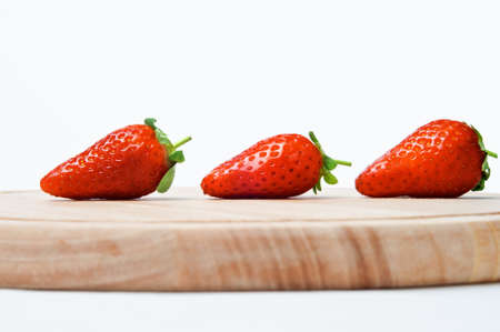 A line of three red strawberries with leaves and short stalks intact.の写真素材
