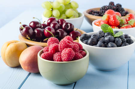 A selection of different Summer fruits, in a variety of bowls on a painted blue wood planked...