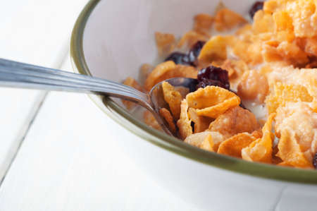 Close up of a bowl of cornflakes and milk, scattered with raisins on a painted wood planked table, with spoon inserted to gather a mouthful to eat.の写真素材
