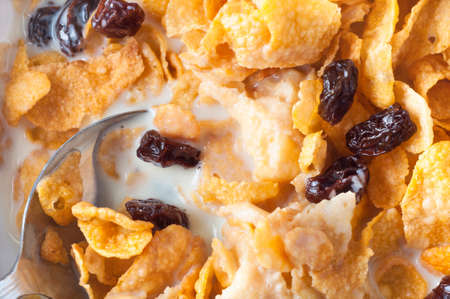 Close up, overhead and shot of cornflakes and raisins cereal breakfast in milk, filling frame with spoon at lower left corner.の写真素材