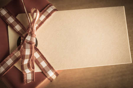 A vintage style desaturated red gift box for Christmas, with gingham ribbon tied into a bow. An old parcel tag is used as a label.  Shot overhead so label is facing upwards towards the viewer and left blank to provide copy space. の写真素材