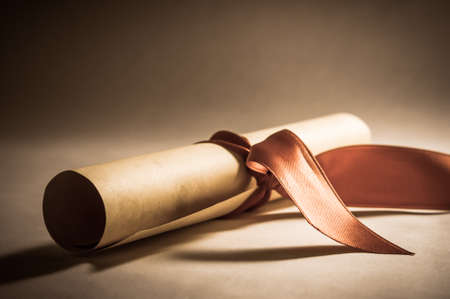 A parchment diploma scroll, rolled up with red ribbon laid at an oblique angle.  Processed to give a vintage or retro appearance.の写真素材