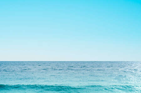 Background image of sea and sky with wave forming towards the front of the image.  Clear blue sky and calm weather.の写真素材