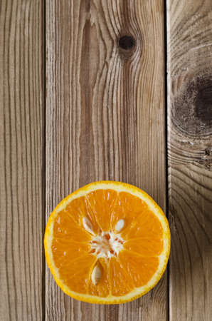 Overhead shot of an orange half with cut side facing upwards, flesh and pips exposed.  Set at bottom of frame on a wood planked surface that has been slightly desaturated for a grungy effect.の写真素材