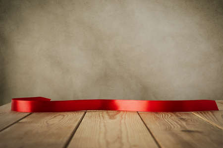 A red satin ribbon, curved and facing front to provide copy space for message, placed on a wood plank table against parchment background.  Vintage style.の写真素材