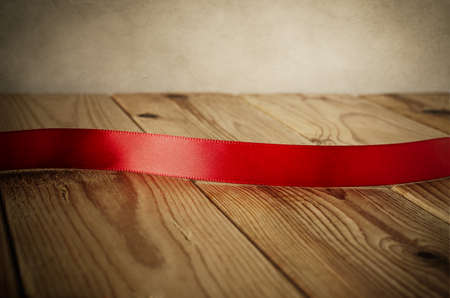 Close up of a red satin ribbon on an old wood plank table. Facing front to provide copy space for a message.  Parchment background.  Vintage style.の写真素材