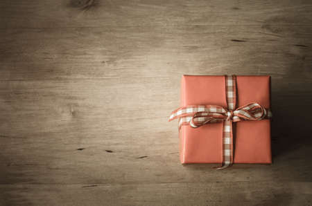 A square gift box, tied with gingham check ribbon, shot from above on wooden planked table.  Vintage style colouring and vignette applied.  Copy space on left side.の写真素材