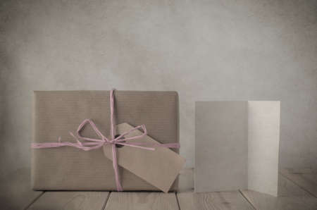 Photograph with vintage treatment of a gift box wrapped in brown paper, tied to a bow with with pale pink raffia and with blank parcel tag label facing frontの写真素材