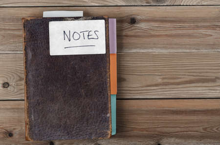 Overhead shot of an old, weathered brown notebook updated with colourful new tab dividers along side and bookmark poking out from topの写真素材