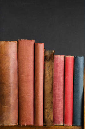 Wooden bookshelf with row of battered old vintage books standing upright.  Blank spines and...