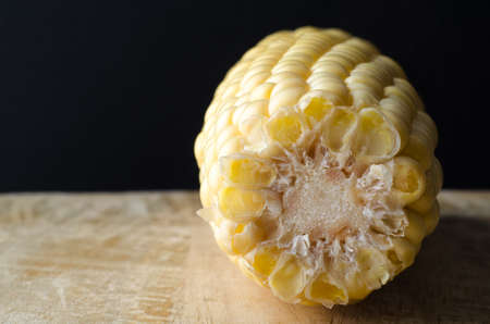 A sweetcorn cob, with end facing viewer, on a wooden table against a black chalkboard background.の写真素材