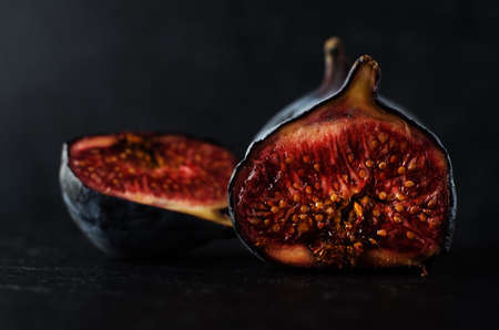 Close up of well ripened figs, cut open to expose seeds and juicy innards.  Still life composition on black slate with black background.の写真素材