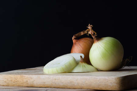 Still life arrangement of onions, whole, sliced, peeled and unpeeled on a wooden kitchen chopping board against a black background.の写真素材