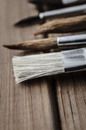 Close up of a variety of artist's paintbrushes, lying on a wood plank table.