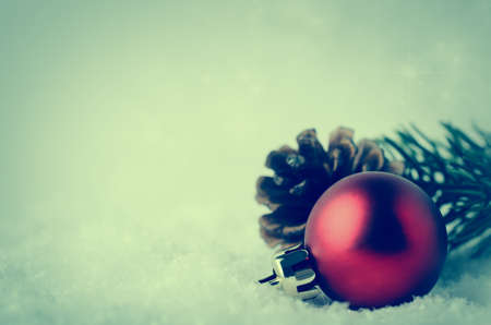 A Christmas border and background with red bauble, fir cone and green branch, nestling in white fake snow in lower right corner.  Twinkling stars in background above. Cross processed for retro or vitnage effect.の写真素材
