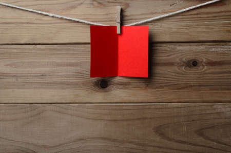 A blank, red greetings or Christmas card, pegged to string against old wood planked background. ...