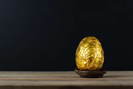 Easter concept.  A chocolate egg, wrapped in crinkled metallic gold foil.の写真素材
