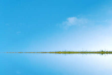 Background image of a blue sky reflected in water (artificial), divided by grassy green strip of land, sprinkled with yellow buttercups.の写真素材